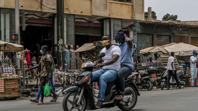 Mit Schutzmaske unterwegs auf dem Motorroller in Dakar.