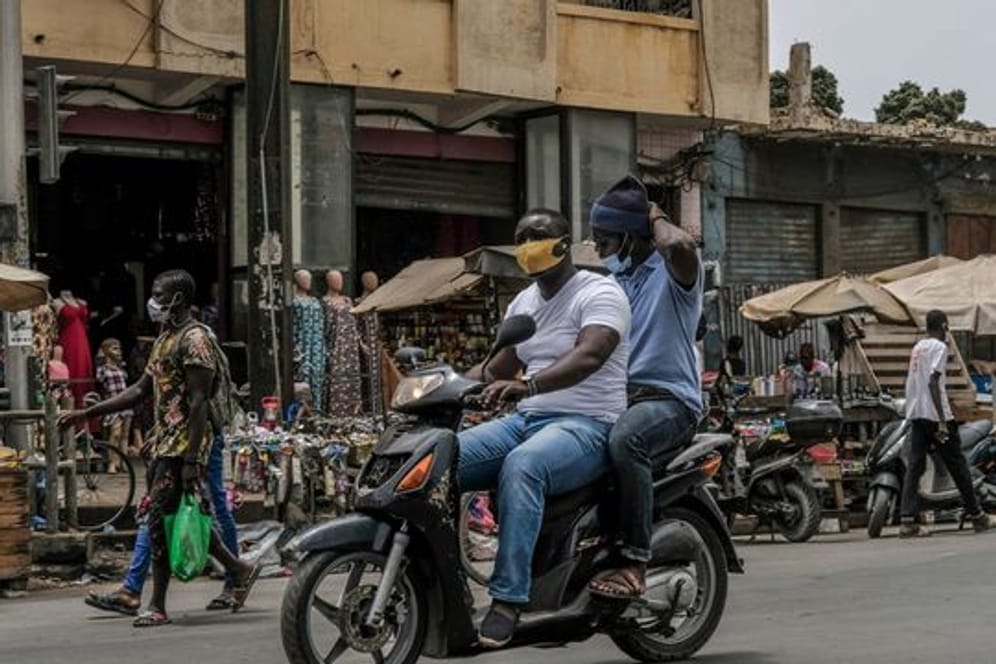 Mit Schutzmaske unterwegs auf dem Motorroller in Dakar.