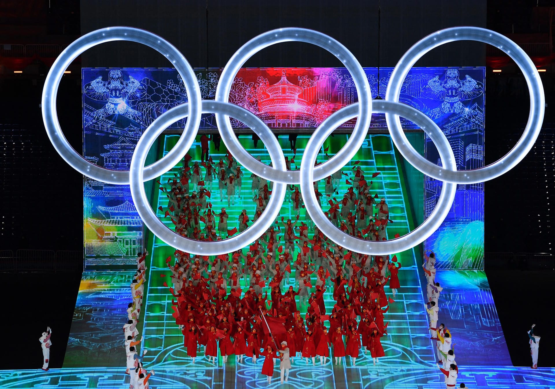 Das Gastgeberland betritt die Fläche, es gibt Applaus von Präsident Xi Jinping: Darüber prangen die olympischen Ringe. Gleich startet die Rede von IOC-Präsident Thomas Bach.