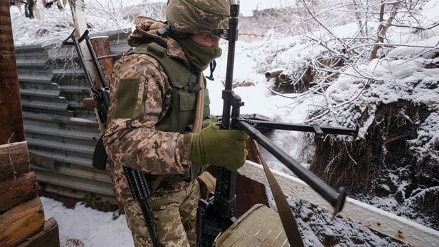 Ein ukrainischer Soldat trägt in einem Graben an der Frontlinie in der Ostukraine ein schweres Maschinengewehr.