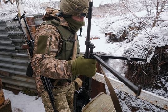 Ein ukrainischer Soldat trägt in einem Graben an der Frontlinie in der Ostukraine ein schweres Maschinengewehr.