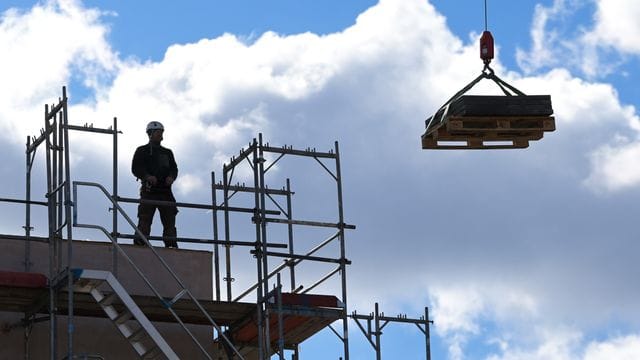 Ein Arbeiter dirigiert auf einer Baustelle einen Kran