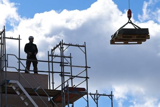 Ein Arbeiter dirigiert auf einer Baustelle einen Kran