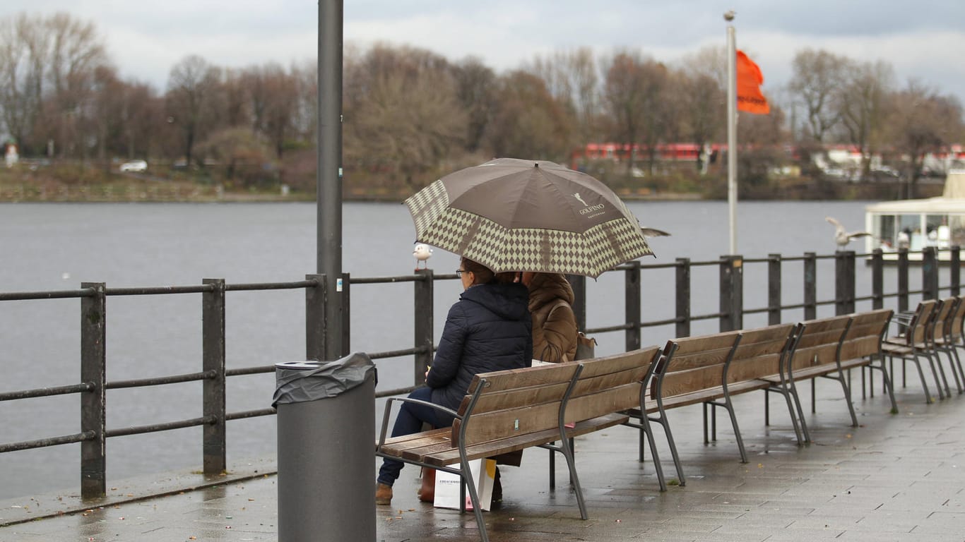 Zwei Frauen sitzen unter einem Regenschirm auf einer Bank an der Binnenalster (Archivbild): Das Regensoll für Hamburg ist für Februar schon bei 100 Prozent.