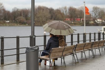 Zwei Frauen sitzen unter einem Regenschirm auf einer Bank an der Binnenalster (Archivbild): Das Regensoll für Hamburg ist für Februar schon bei 100 Prozent.