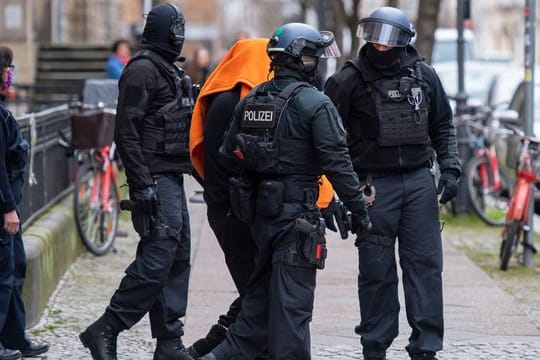Polizisten bringen den Angeklagten unter einer Decke aus dem Gerichtsgebäude in Berlin.