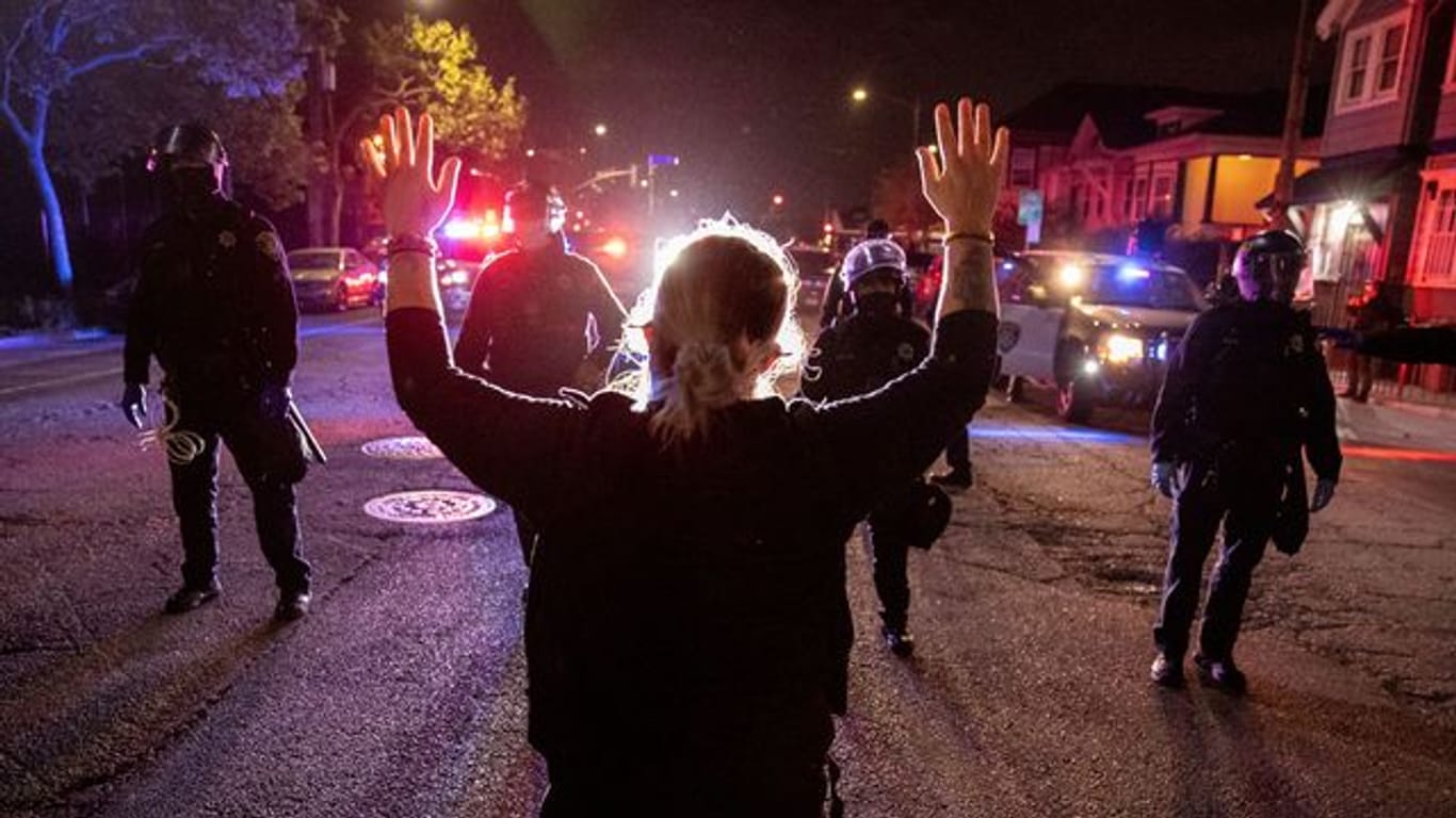 Eine Demonstrantin steht bei einem Protest gegen Polizeigewalt in Oakland mit hochgestreckten Armen vor Polizisten.