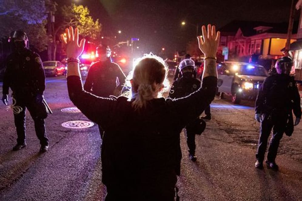 Eine Demonstrantin steht bei einem Protest gegen Polizeigewalt in Oakland mit hochgestreckten Armen vor Polizisten.
