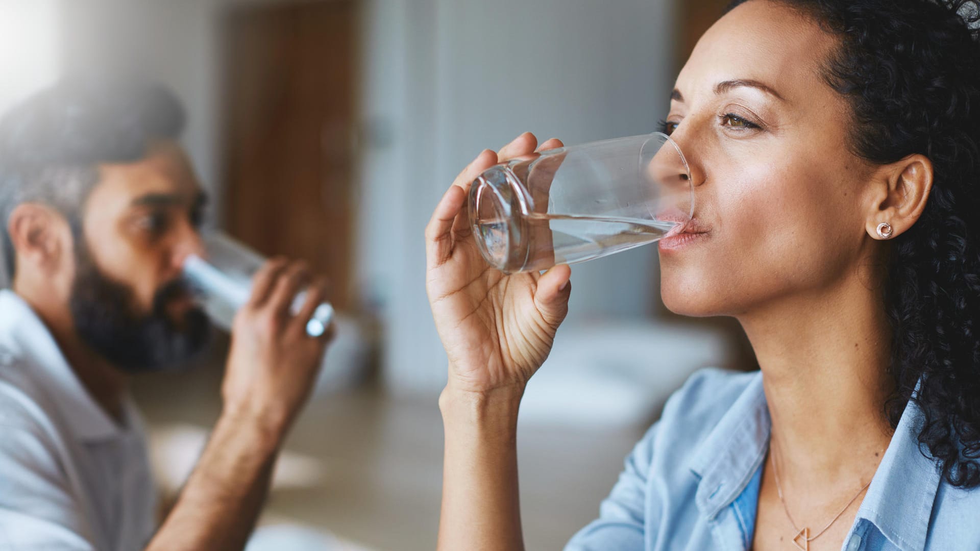 Paar trinkt gemeinsam zuhause Wasser: Viel Wasser trinken: Flüssigkeitszufuhr ist bei Inkontinenz und Blasenschwäche wichtig. Leider verzichten viele Betroffene darauf, ausreichend zu trinken. Die Angst vor einen verstärkten Harndrang ist zu groß. Doch ein Flüssigkeitsmangel reizt Blase nur und kann das Problem noch verschlimmern.