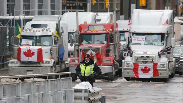 Ein Polizeibeamter steht vor Lastwagen, die die Straßen der Innenstadt von Ottawa blockieren.