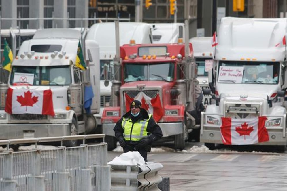Ein Polizeibeamter steht vor Lastwagen, die die Straßen der Innenstadt von Ottawa blockieren.