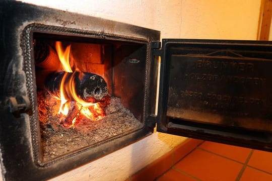 Ein Holzofen wird vom Hausflur aus mit Holzbriketts geheizt.