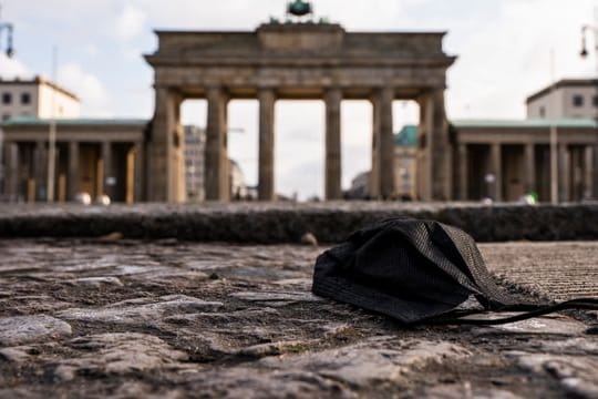 Eine schwarze Corona-Makse liegt auf dem Boden vor dem Brandenburger Tor.
