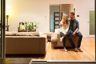 Ein Paar sitzt in seinem Wohnzimmer (Symbolbild): Je mehr Vermögen Sie selbst für den Hauskauf einsetzen können, desto günstiger die Finanzierung.