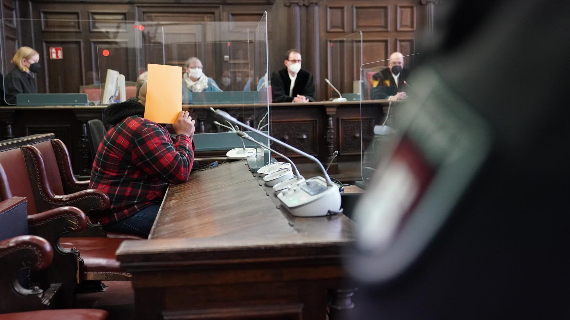Der Angeklagte sitzt mit einer Mappe vor dem Gesicht im Gerichtssaal: Der Mann stürzte wohl mit dem Kind auf dem Arm und schüttelte es daraufhin. Der Angeklagte sitzt mit einer Mappe vor dem Gesicht im Gerichtssaal: Der Mann stürzte wohl mit dem Kind auf dem Arm und schüttelte es daraufhin.