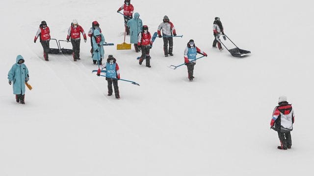 Helfer versuchen die Slopestyle-Piste vom Schnee zu befreien.