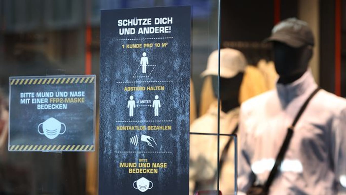 Ein Bekleidungsgeschäft in Augsburg weist auf verschiedene Corona-Regeln hin.