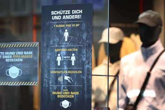 Ein Bekleidungsgeschäft in Augsburg weist auf verschiedene Corona-Regeln hin.