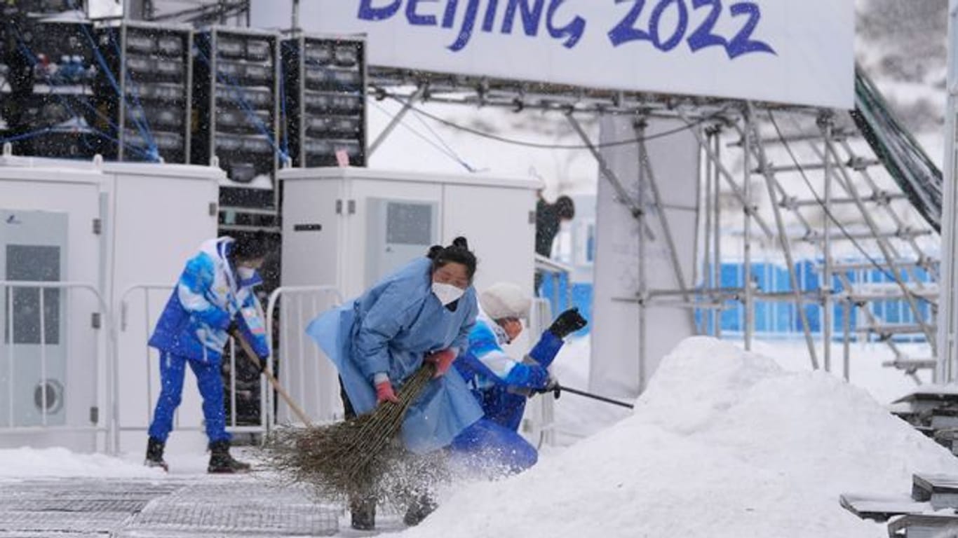 Im Nationalen Biathlonzentrum fegen Olympia-Mitarbeiter Schnee: Der Start der Männer-Biathlon-Staffel wird wegen Kälte verlegt.