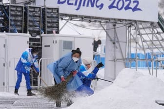 Im Nationalen Biathlonzentrum fegen Olympia-Mitarbeiter Schnee: Der Start der Männer-Biathlon-Staffel wird wegen Kälte verlegt.