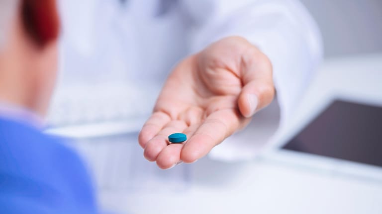 Arzt zeigt einem Patienten eine blaue Tablette.