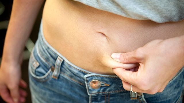 Eine Frau zwickt sich in den Bauch: Verschiedene Formen der Essstörung nehmen vor allem bei jungen Mädchen zu.