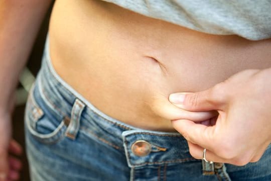 Eine Frau zwickt sich in den Bauch: Verschiedene Formen der Essstörung nehmen vor allem bei jungen Mädchen zu.