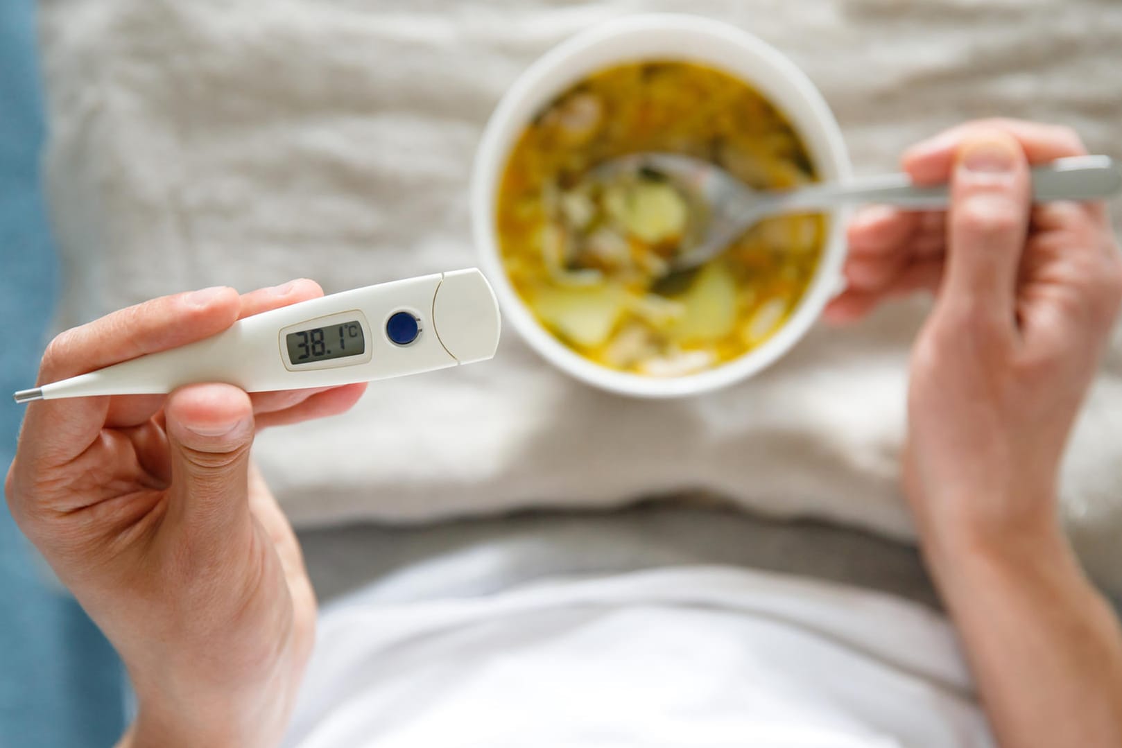 Mann mit Grippe isst Hühnersuppe im Bett: Die Hühnersuppe ist der Klassiker unter den Erkältungs-Suppen. Ausreichend Nährstoffe stärken die Immunabwehr und unterstützen die Regeneration.