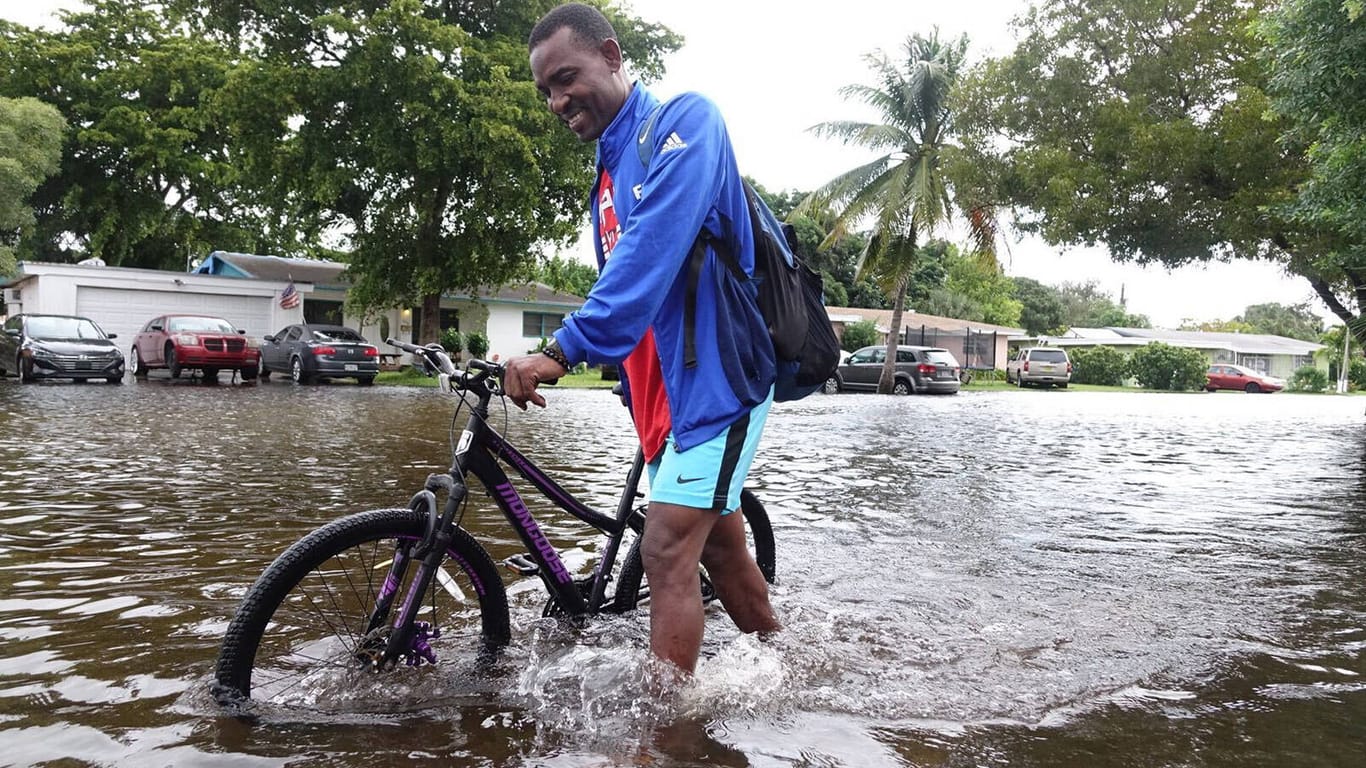 Ein Mann schiebt sein Rad durch Hochwasser in Florida (Archivbild): Die Nasa erwartet in den Küstengebieten mehr Überschwemmungen durch den Meeresspiegelanstieg.