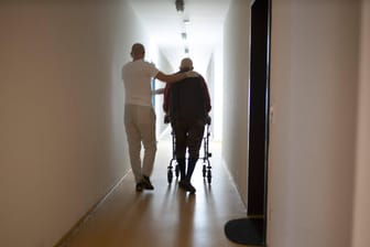 Altenpfleger und Mann mit Rollator im Hausflur (Symbolbild): Der Notstand in der Pflege ist laut Krankenkasseninformationen in Bayern größer als gedacht.