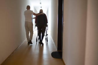 Altenpfleger und Mann mit Rollator im Hausflur (Symbolbild): Der Notstand in der Pflege ist laut Krankenkasseninformationen in Bayern größer als gedacht.