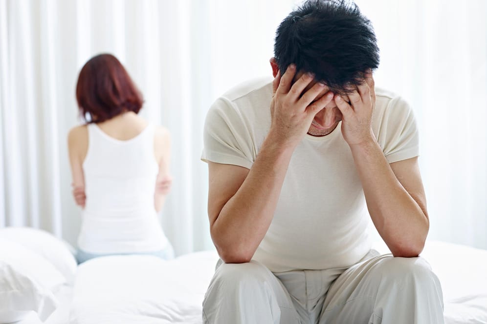 Paar sitzt frustriert auf dem Bett: Stress in der Partnerschaft kann die Ursache dafür sein, dass es im Bett nicht mehr klappt.