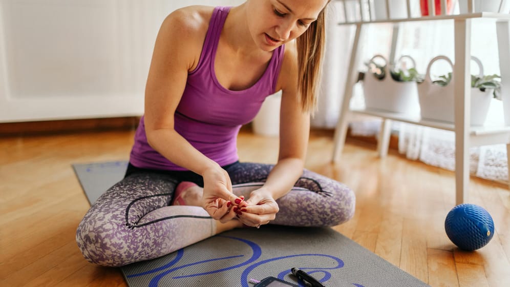 Sportliche Frau misst ihren Blutzuckerspiegel: Sport hilft den Blutzuckerspiegel zu senken und eine Diabetes-Erkrankung zu stabilisieren. Jedoch sollte die Bewegungsintensität schonend sein, um eine Unterzuckerung zu vermeiden.