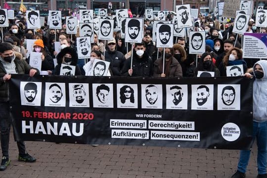 Mit Plakaten und Bildern der Ermordeten erinnern Teilnehmer einer Gedenkveranstaltung auf dem Marktplatz von Hanau an die Opfer der Anschläge von Hanau.