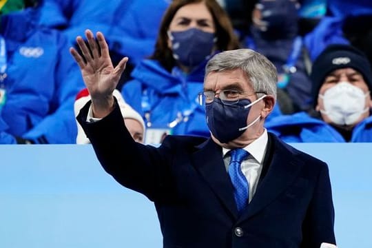 IOC-Präsident Thomas Bach (M) winkt bei der Eröffnungsfeier der Olympischen Winterspiele von der Tribüne aus.