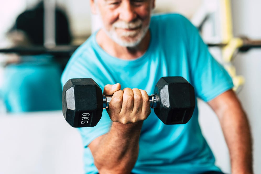 Ein älterer Mann hebt Gewichte. KrModerates Krafttraining bei Arthrose stärkt die Muskulatur und wirkt dem Knorpelabbau entgegen.