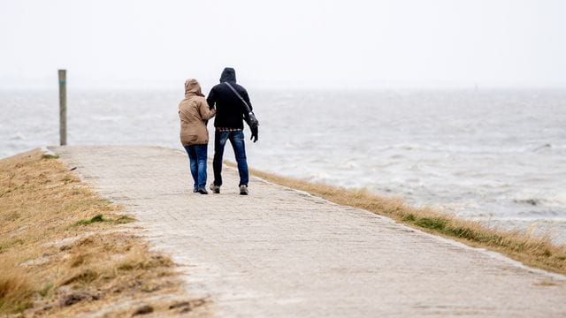 Ein Mann und eine Frau gehen bei starkem Wind über eine Mole Ein Mann und eine Frau gehen bei starkem Wind über eine Mole