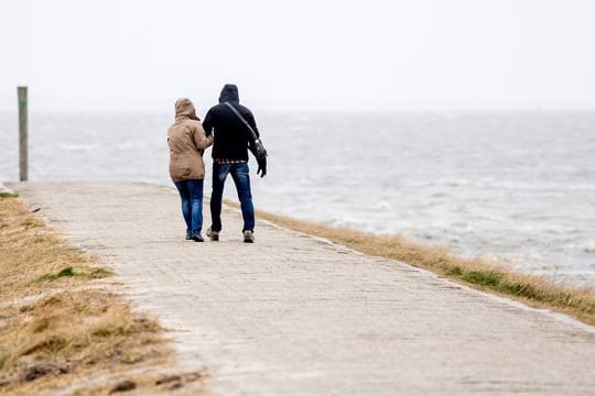 Ein Mann und eine Frau gehen bei starkem Wind über eine Mole