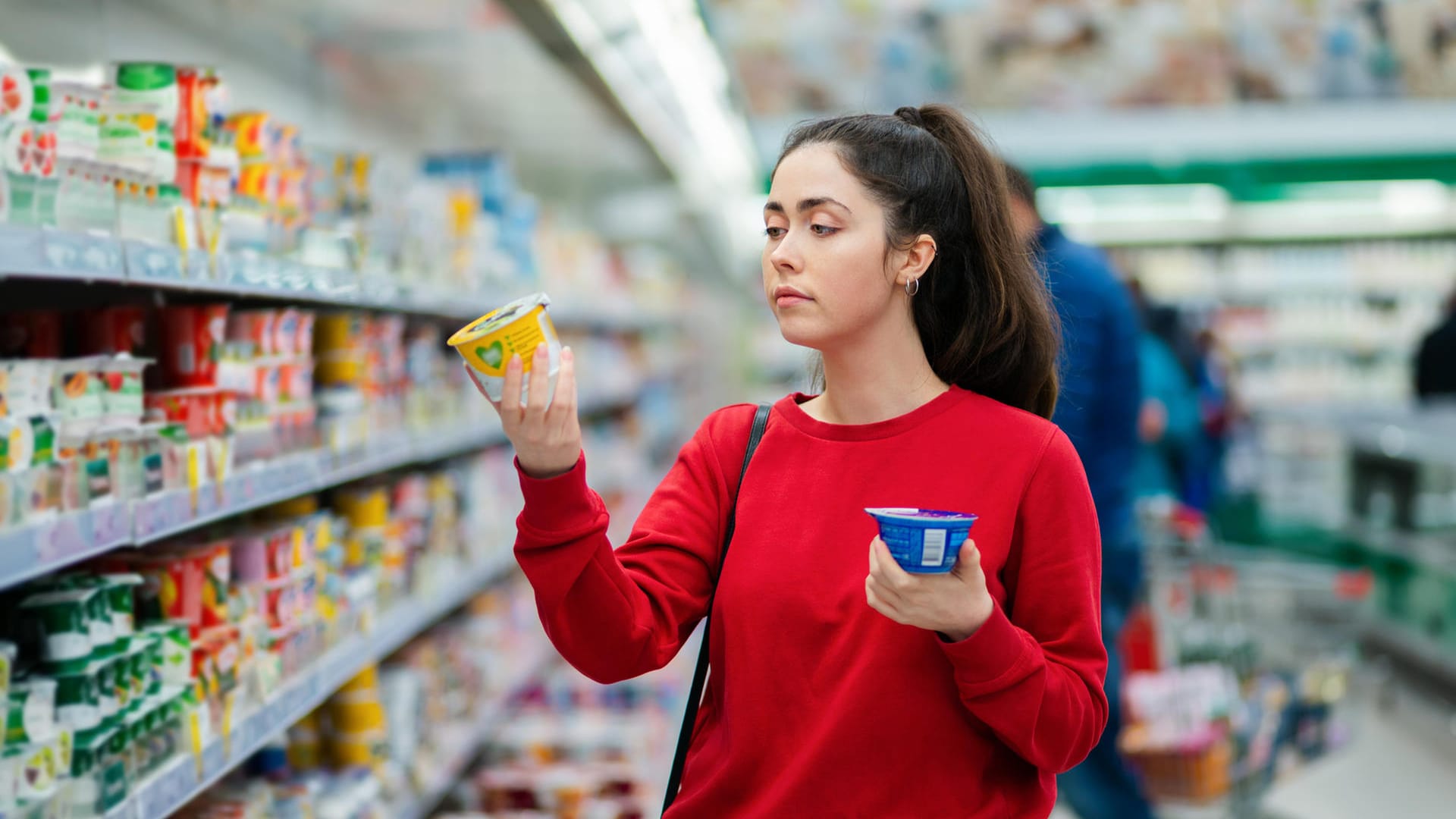 Eine junge Frau vergleicht Joghurt (Symbolbild): Bei einer Gehaltserhöhung steigt Ihr Nettoeinkommen nicht im gleichen Maß wie Ihr Bruttoeinkommen.