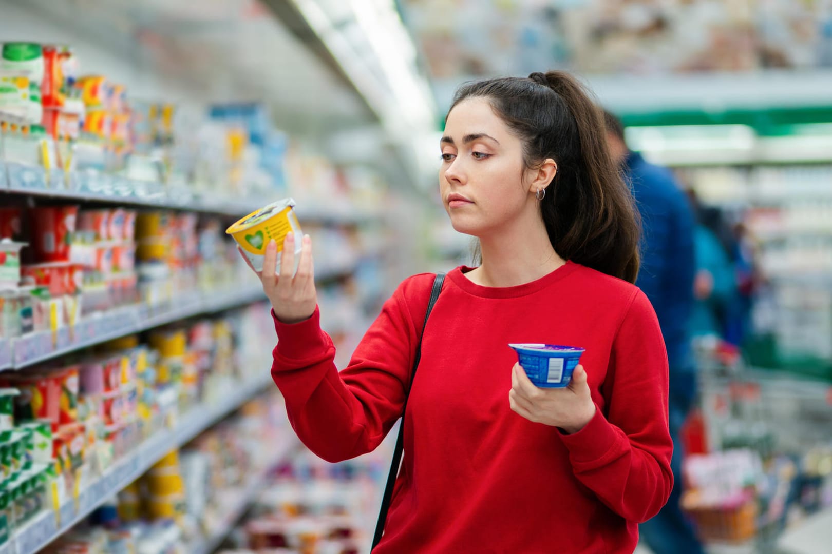 Eine junge Frau vergleicht Joghurt (Symbolbild): Bei einer Gehaltserhöhung steigt Ihr Nettoeinkommen nicht im gleichen Maß wie Ihr Bruttoeinkommen.