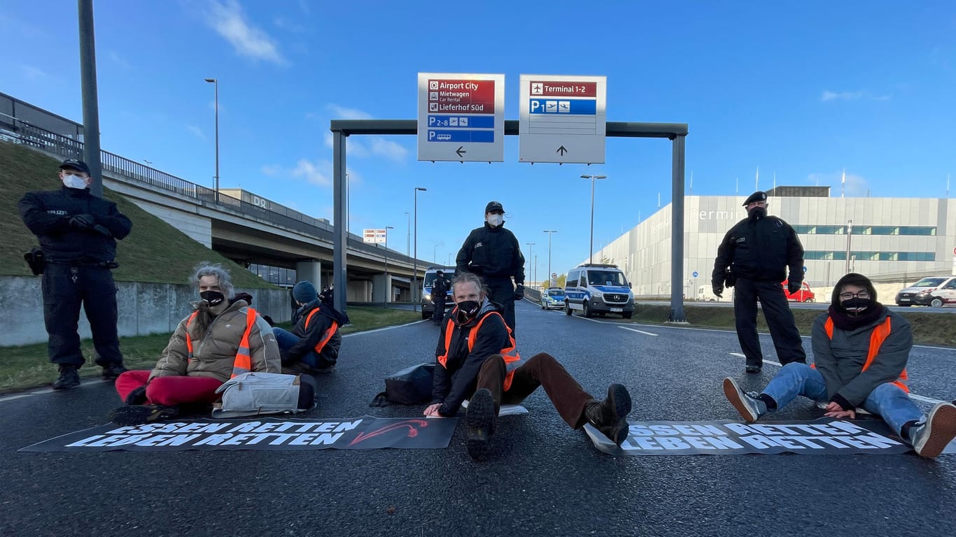Aktivisten der Initiative "Aufstand der letzten Generation" blockieren eine Zufahrt zum Hauptstadt-Flughafen BER: Seit Wochen sorgen sie mit ihren Aktionen für Aufsehen – und Unverständnis bei Bürgern und Politik.