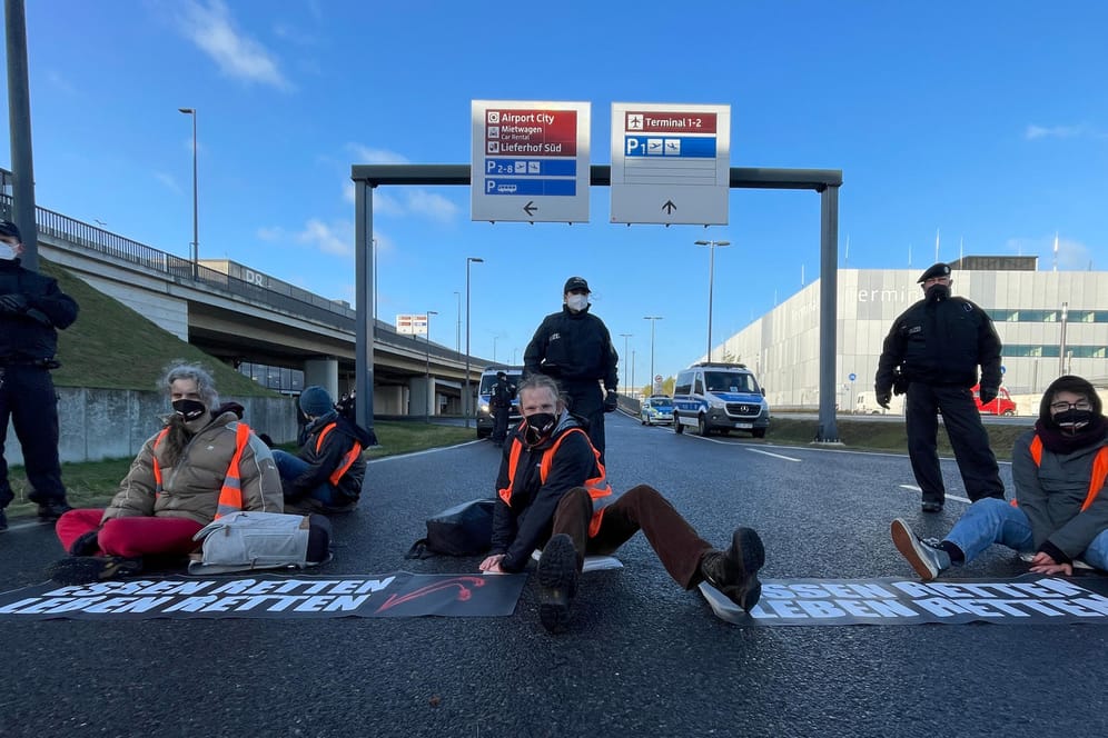 Aktivisten der Initiative "Aufstand der letzten Generation" blockieren eine Zufahrt zum Hauptstadt-Flughafen BER: Seit Wochen sorgen sie mit ihren Aktionen für Aufsehen – und Unverständnis bei Bürgern und Politik.