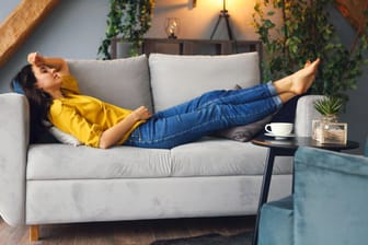 Eine junge Frau entspannt auf dem Sofa (Symbolbild): Wer wiederholt vortäuscht, arbeitsunfähig zu sein, riskiert eine Abmahnung.