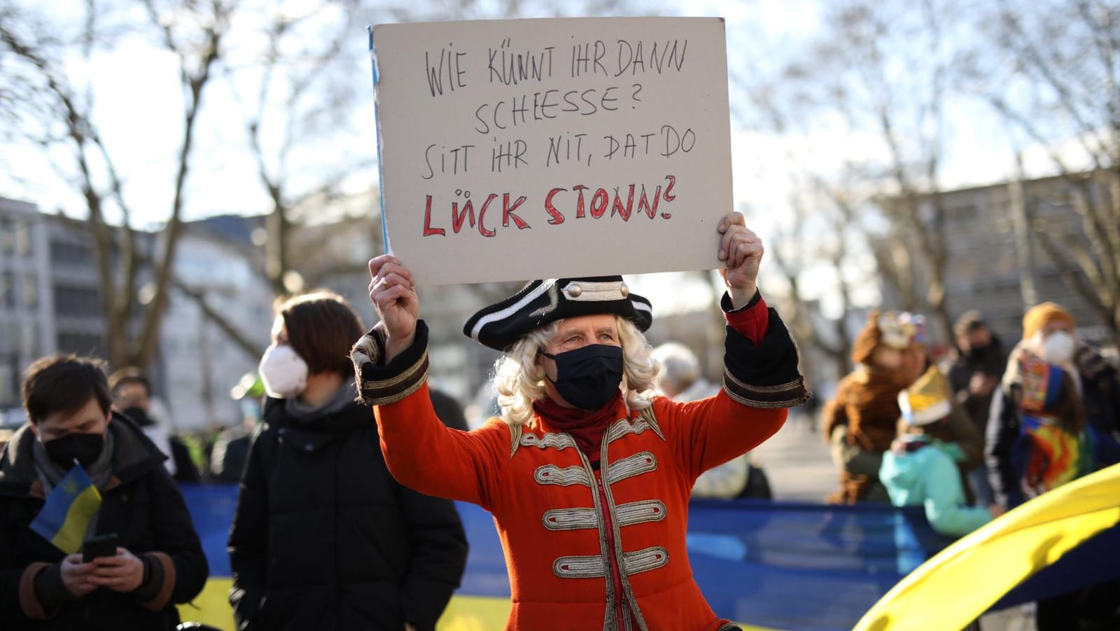 Solidaritätsbekundung mit den Opfern des russischen Kriegs: "Wie könnt ihr denn schießen? Seht ihr nicht, dass da Leute stehen?", steht auf dem Schild dieses verkleideten Mannes.