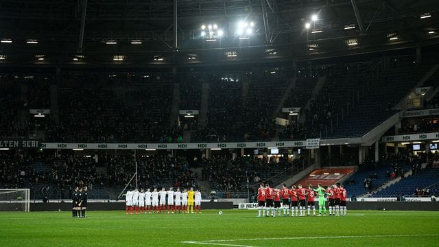 Die Mannschaften von Hannover 96 und Holstein Kiel stehen vor dem Spiel während einer Gedenkminute für die Ukraine auf dem Feld.