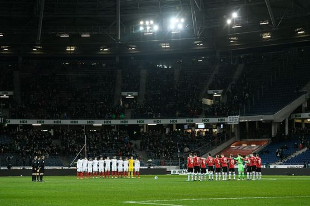 Die Mannschaften von Hannover 96 und Holstein Kiel stehen vor dem Spiel während einer Gedenkminute für die Ukraine auf dem Feld.