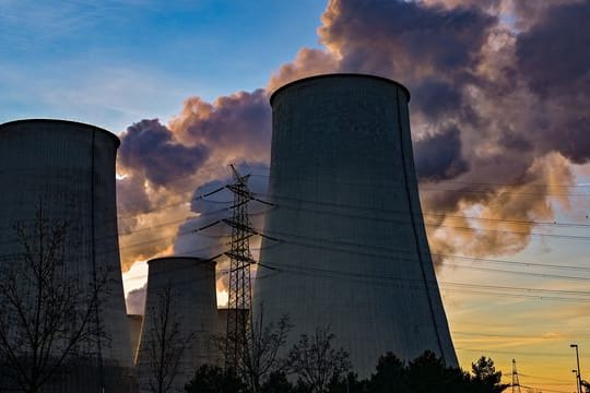 Wasserdampf steigt bei Sonnenuntergang aus den Kühltürmen eines Braunkohlekraftwerks.