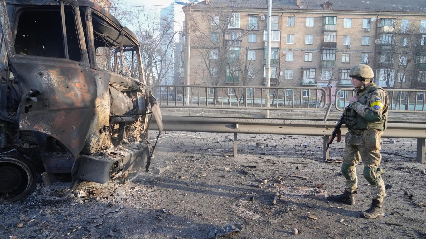 Ein ukrainischer Soldat geht an den Trümmern eines brennenden Militärlastwagens vorbei