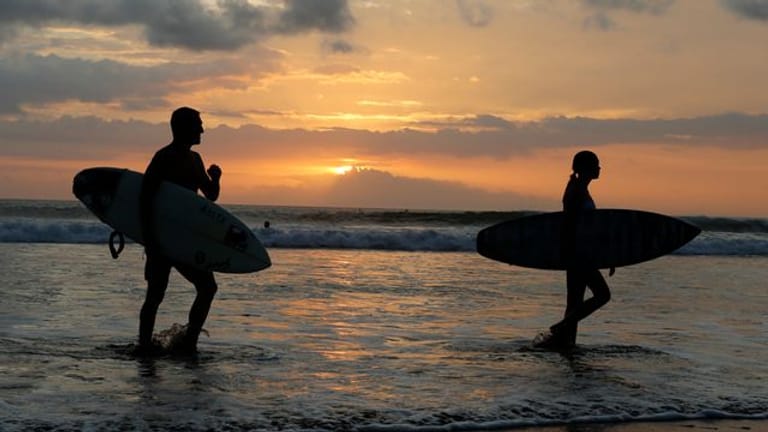 Surfer gehen an einem Strand auf Bali durch seichtes Wasser.