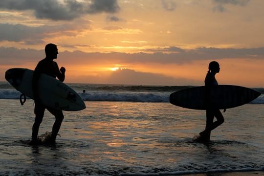 Surfer gehen an einem Strand auf Bali durch seichtes Wasser.